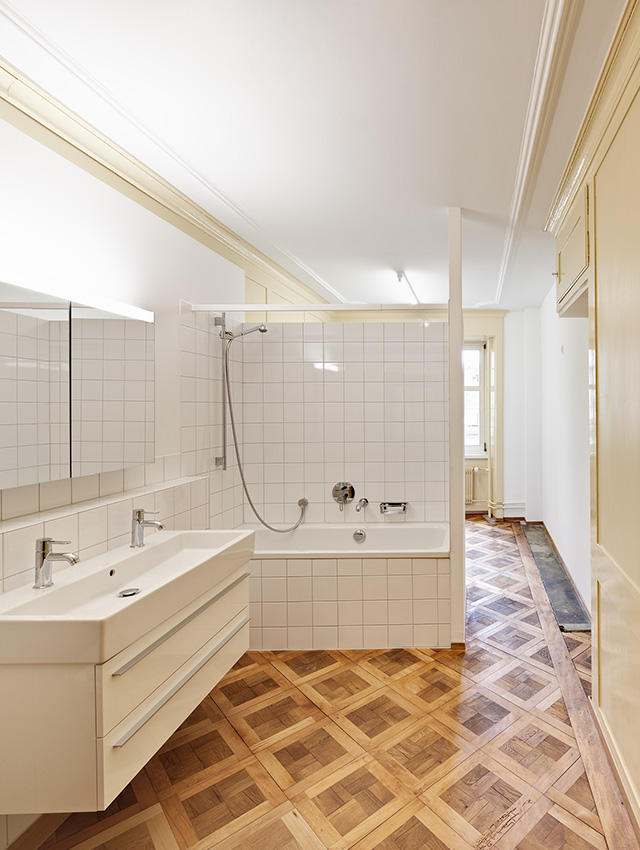 Badezimmer mit Parkettfußboden, weißen Fliesen und Badmöbeln.