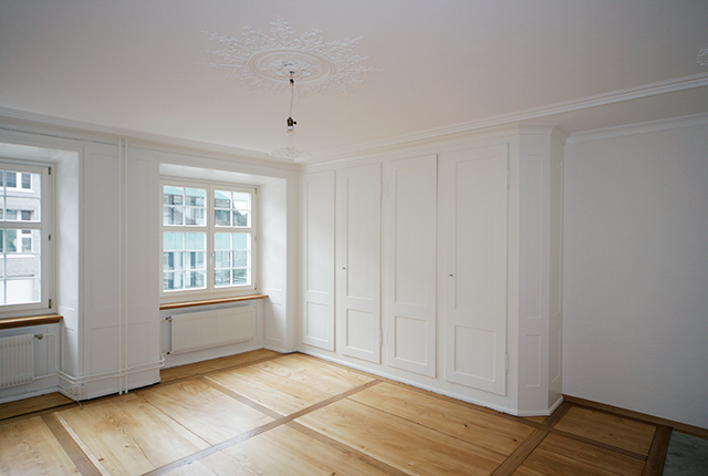 Heller Wohnraum mit weißen Einbauschränken und altem Holzboden.
